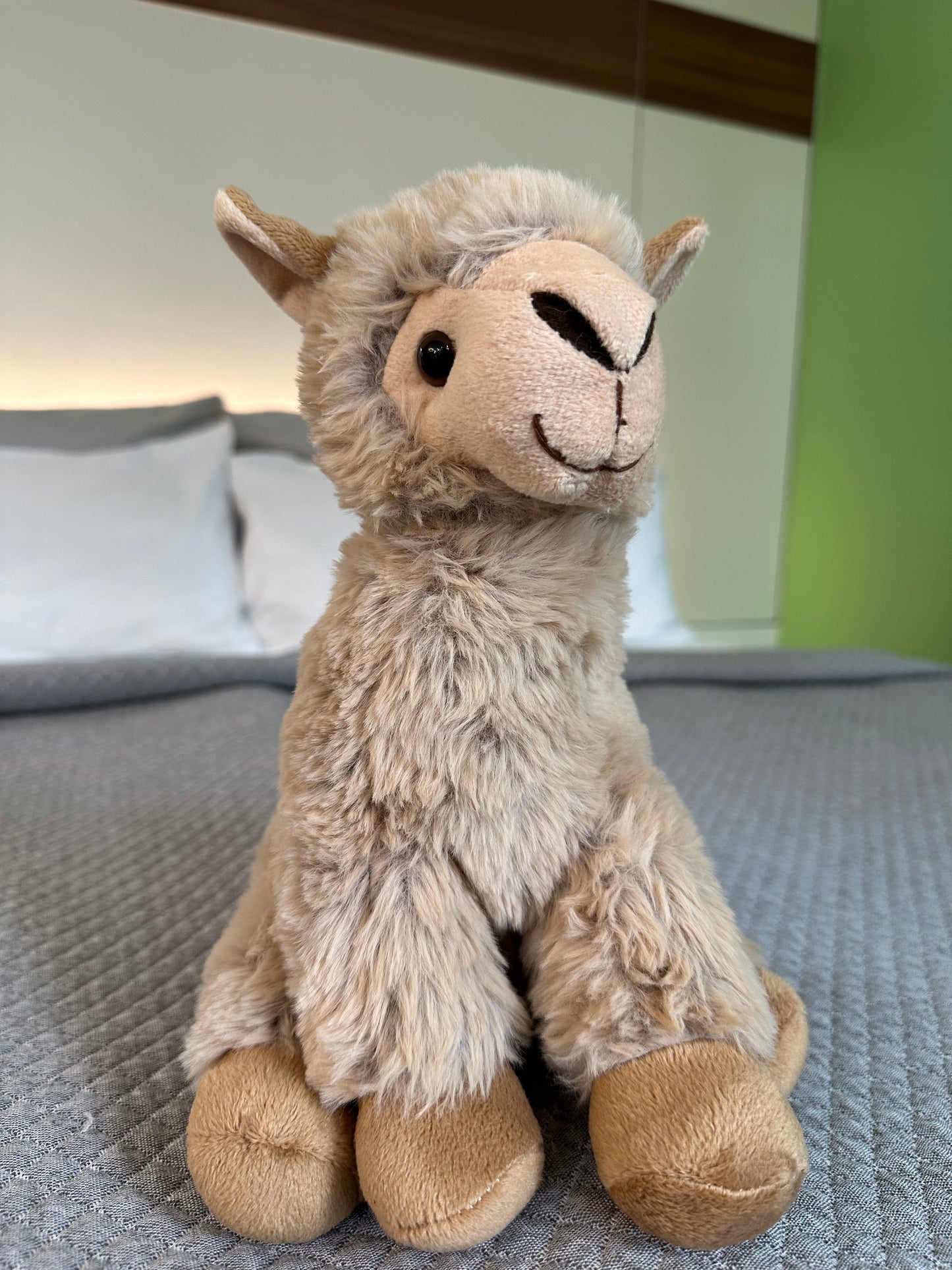 Sitzendes hellbraunes Alpaka Stofftier auf grauer Decke