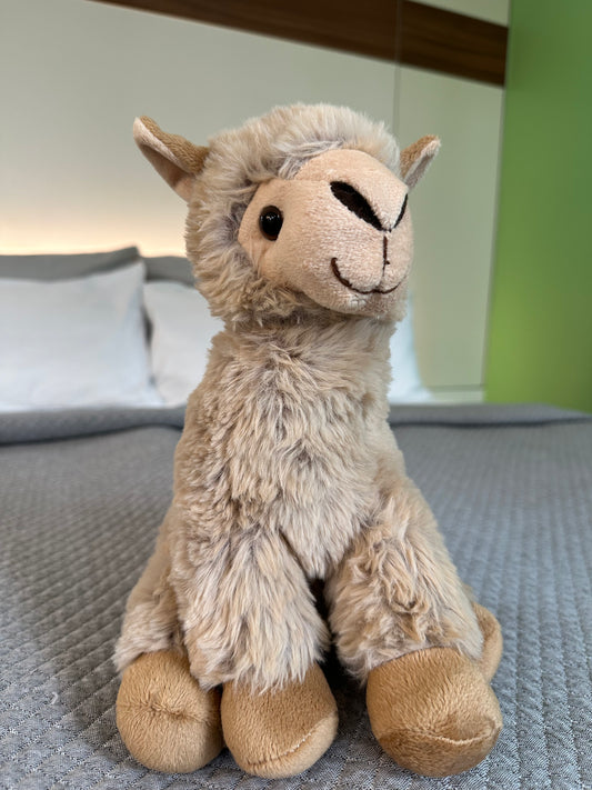 Sitzendes hellbraunes Alpaka Stofftier auf grauer Decke